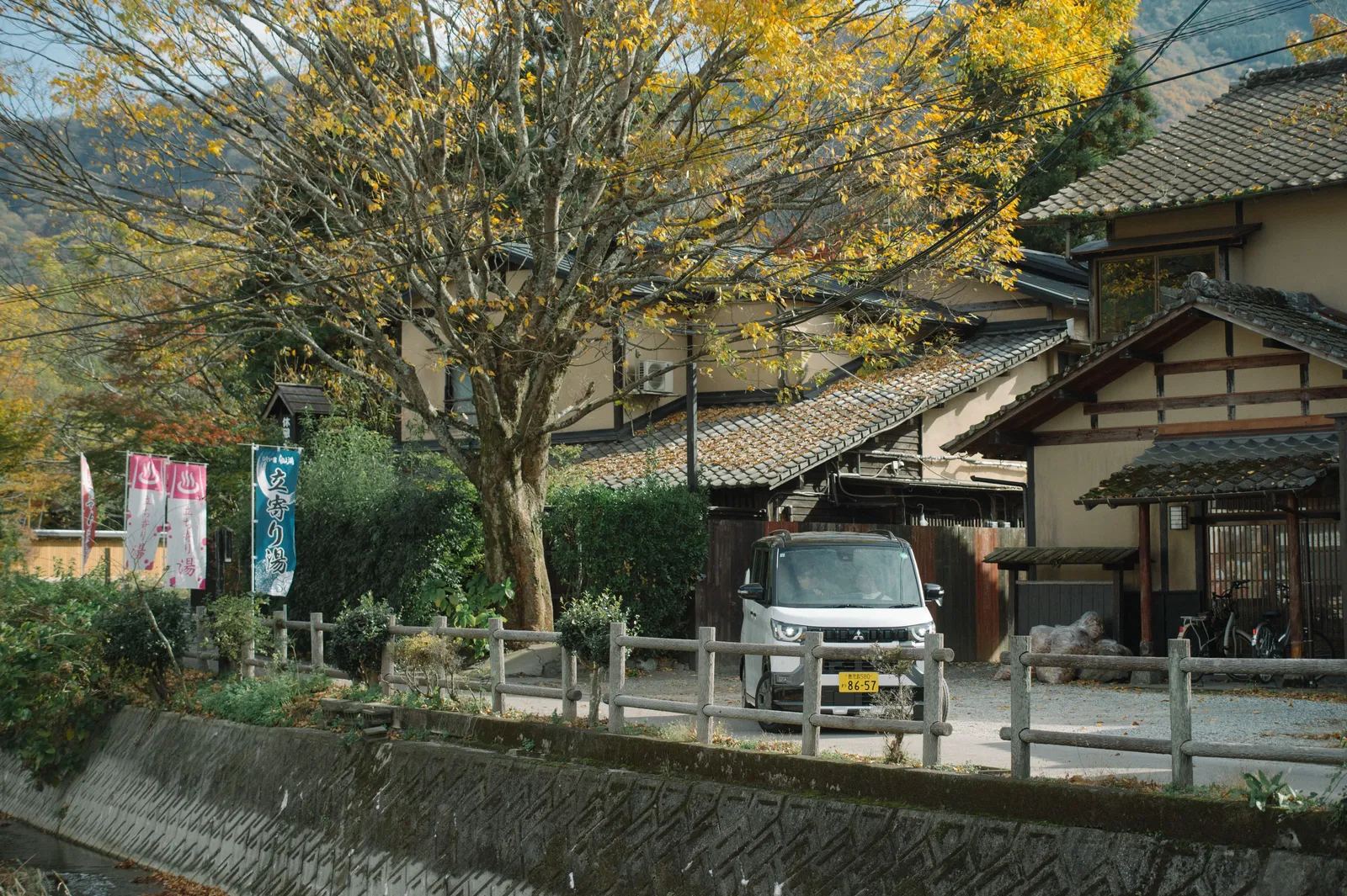 A small van parked on a narrow street beside a stream and traditional buildings in Japan