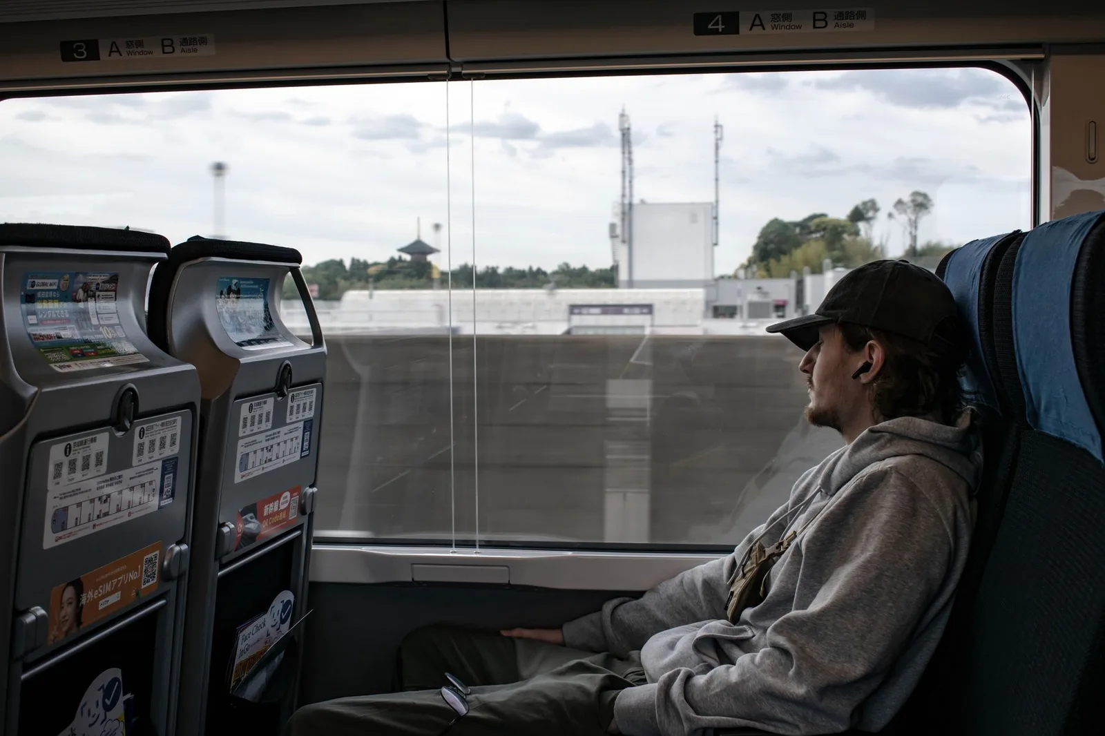 A passenger seated by the window of a Japanese airport express train watching the view go by