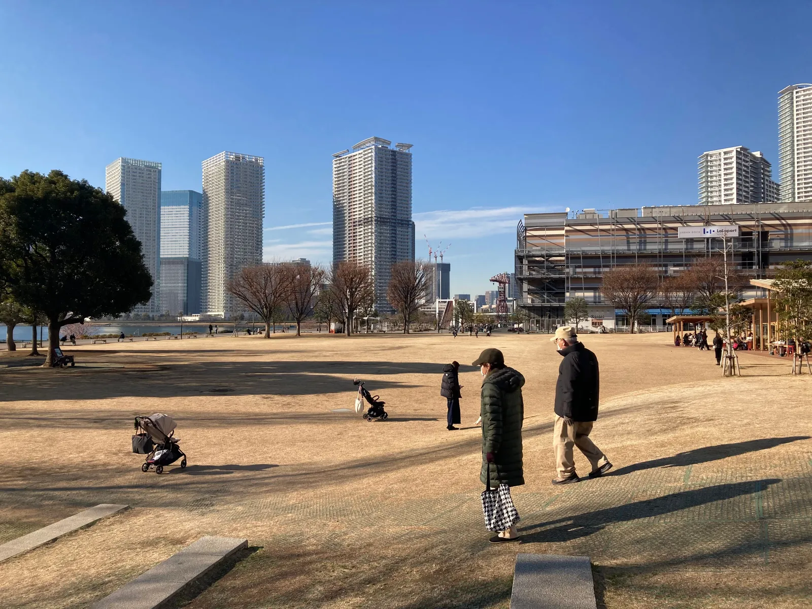 A wide open park plaza in Tokyo with families walking across it and the city towers behind