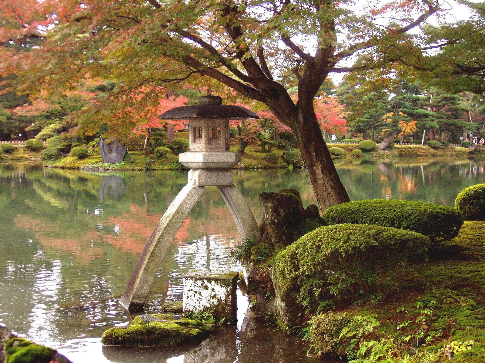 The two legged Kotoji stone lantern at the edge of the pond in Kenrokuen garden, with autumn maples behind it