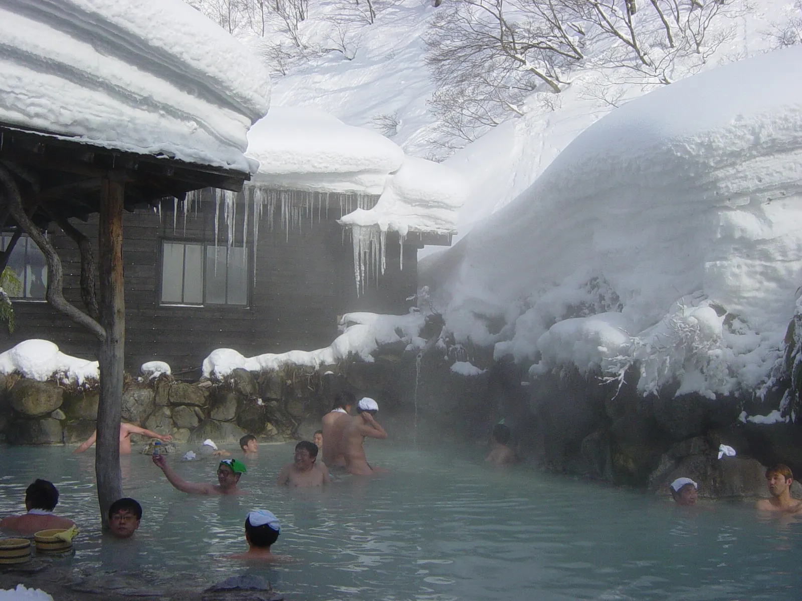 Snow falling gently on a steaming outdoor onsen hot spring surrounded by trees in Japan in winter