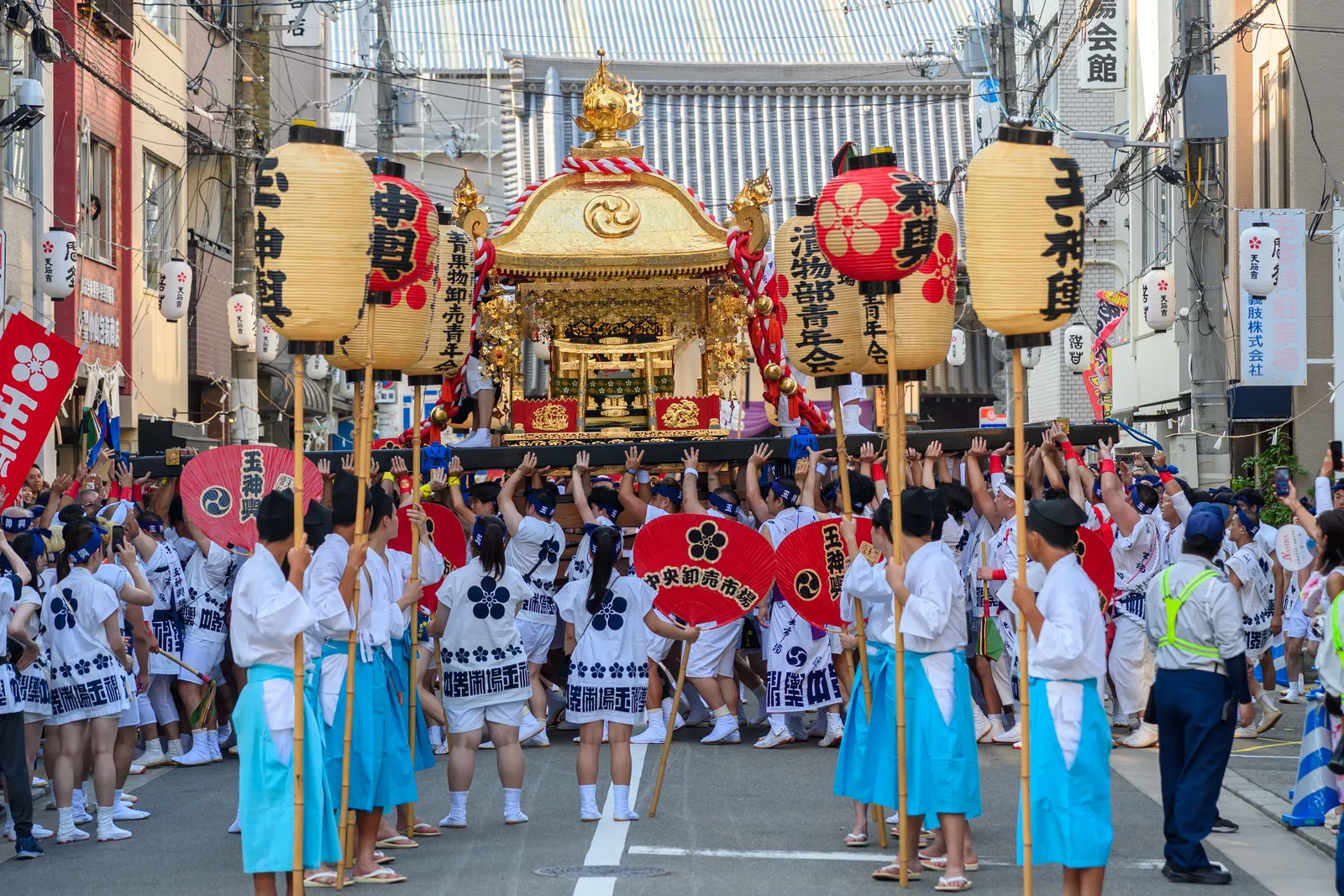 A festival procession carrying a gilded portable shrine through a Japanese street