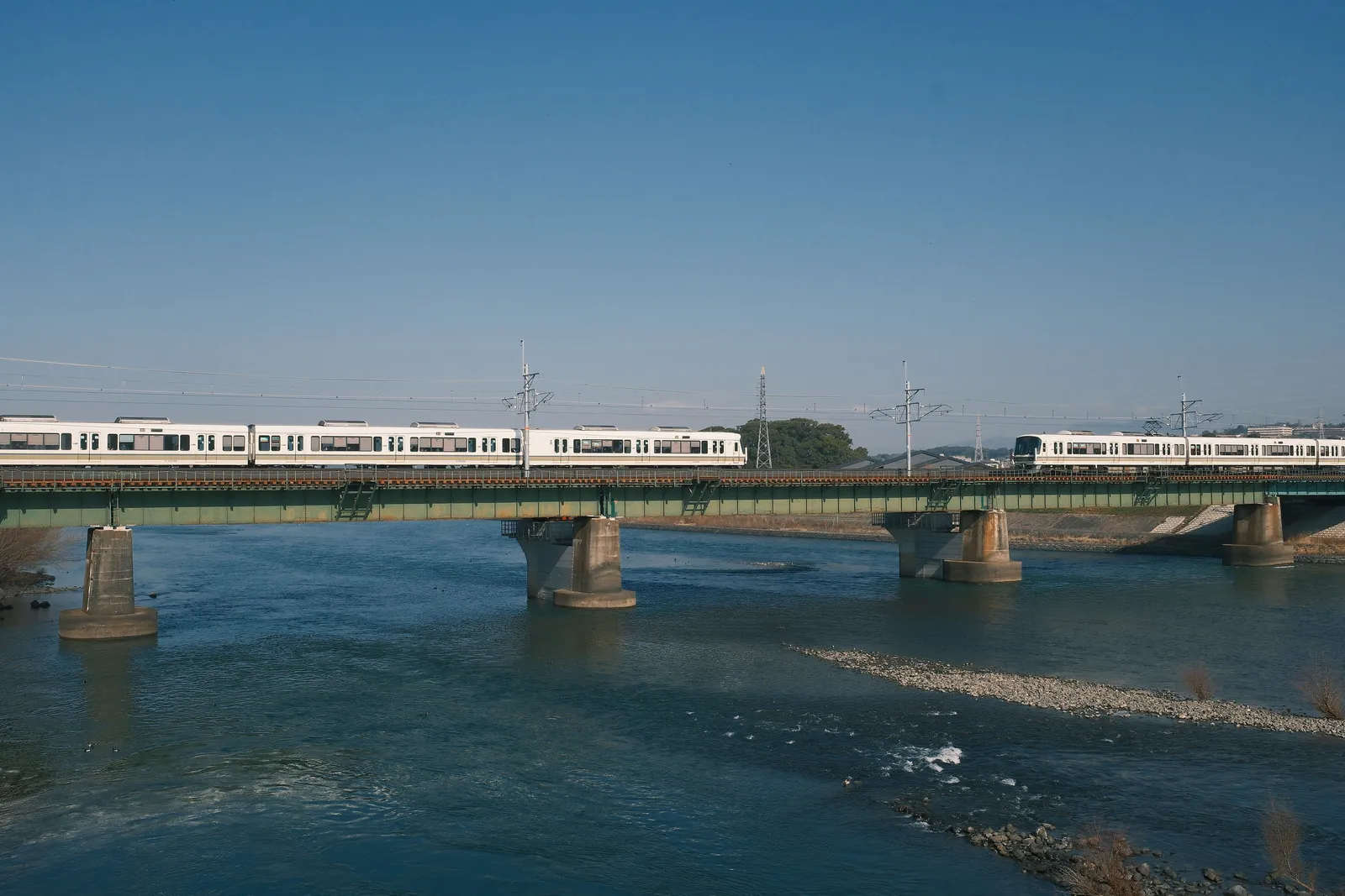 A regional train crossing a bridge over a river in the Japanese countryside
