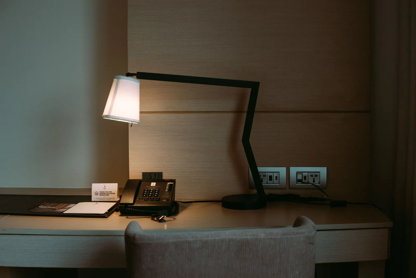 A small dimly lit hotel room with a lamp and a telephone beside the bed